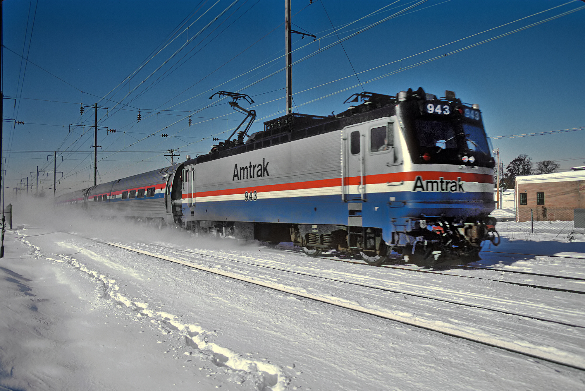 Image of An Amtrak Northeast Corridor train dashes through the Maryland snow in 1987 with the AEM-7 locomotive.